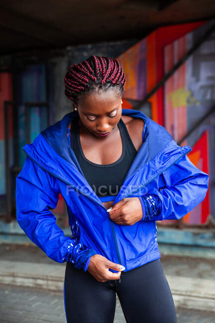 Young African-American athletic woman zipping blue jacket on street — Stock Photo