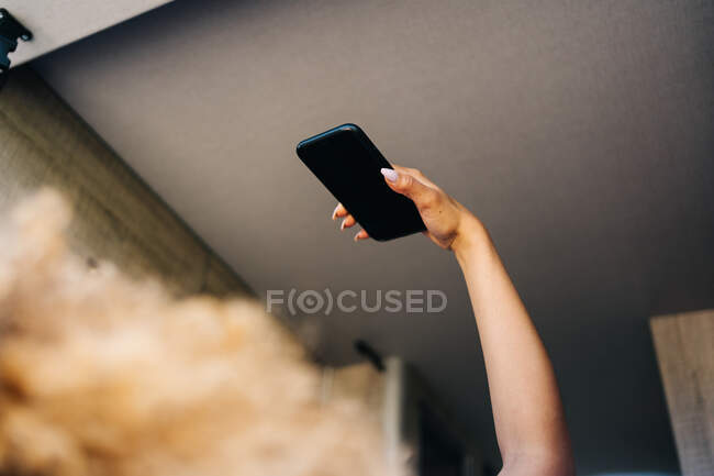 Anonyme Frau mit Afro-Frisur liegt kopfüber auf dem Bett im Wohnwagen und surft an einem sonnigen Sommertag mit dem Handy — Stockfoto