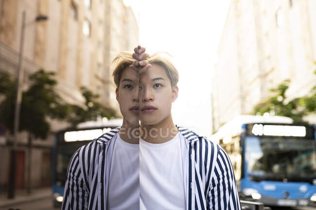 Stylish Asian male model standing near building and reflecting in glass mirrored wall — Stock Photo