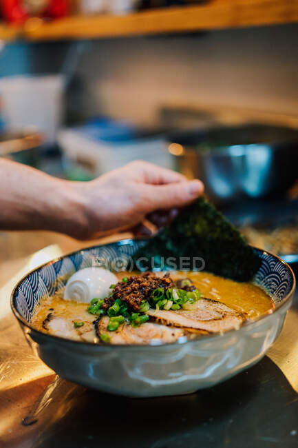 From above of faceless chef cooking traditional ramen with herbs and vegetables in cafe — Stock Photo