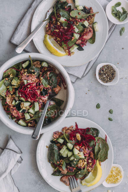 Vista superior de pratos e tigela com salada de lentilha gostosa com pepinos e espinafre colocados perto de guardanapos na mesa cinza — Fotografia de Stock