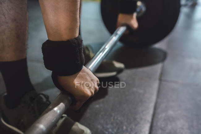 Обрезанный неузнаваемый спортсмен мужского пола, делающий тягу с тяжелой штангой во время тренировки в спортзале — стоковое фото