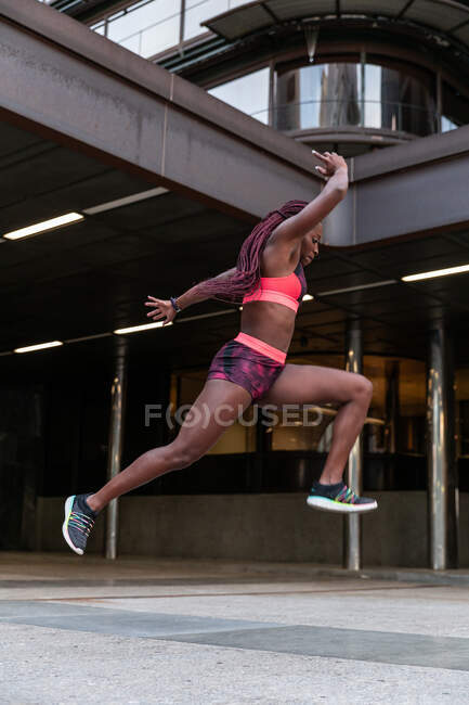 Vista lateral da esportista étnica pulando alto durante o treino na cidade — Fotografia de Stock
