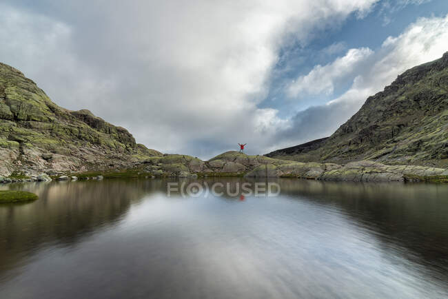 Explorador com braços levantados em uma montanha, enquanto refletido em um lago — Fotografia de Stock