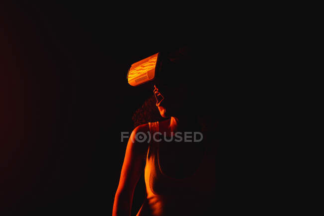 Анонімні дивовижні етнічні жінки з відкритим ротом досліджують віртуальну реальність в гарнітурі на чорному тлі — стокове фото