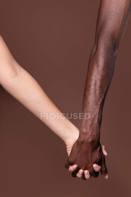 Nahaufnahme einer weißen Frau und eines schwarzen Mannes, die die Hände isoliert auf dunkelbraunem Hintergrund halten; Einheits- und Inklusionskonzept — Stockfoto