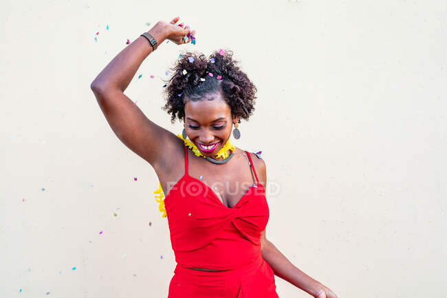Mulher afro-americana excitada com os braços estendidos e boca aberta de pé sob queda confete no evento contra fundo branco — Fotografia de Stock