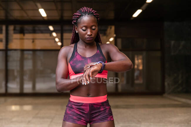 Young muscular ethnic sportswoman setting time on clock while working out on street — Stock Photo