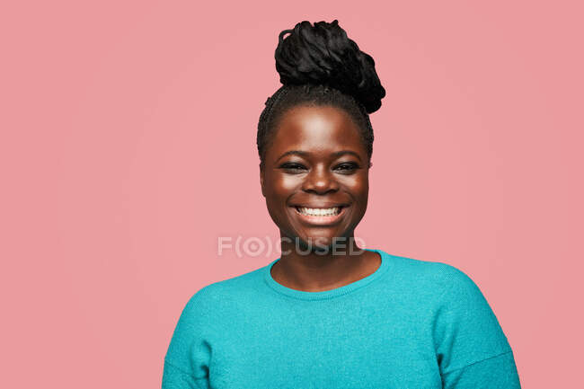 Glad African American femelle en vêtements bleus regardant la caméra debout sur fond rose — Photo de stock