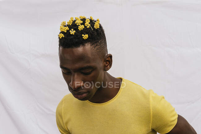 Bello afroamericano maschio con fiori gialli in capelli guardando giù su sfondo bianco — Foto stock