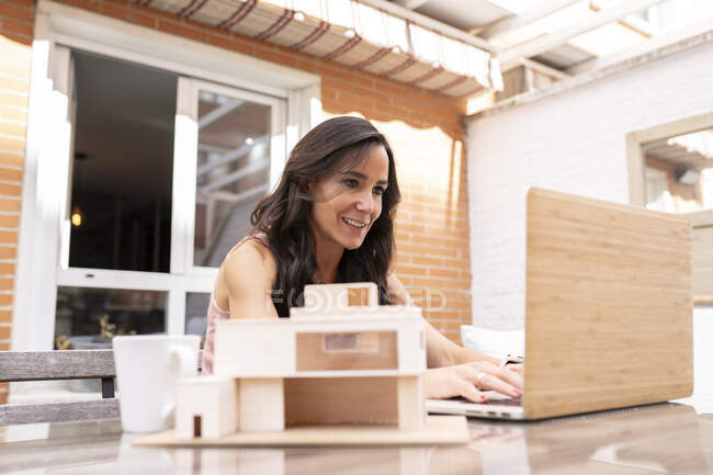 Содержание женщины-фрилансера, сидящей за столом на террасе и печатающей на ноутбуке во время работы над удаленным проектом — стоковое фото