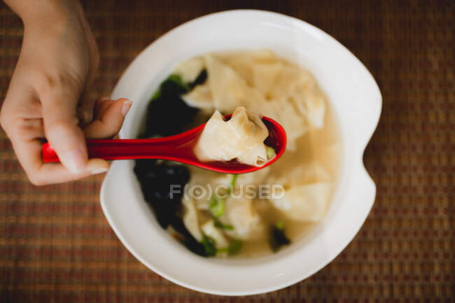 Von oben eine Schüssel mit leckerer heißer Wonton-Suppe mit rotem Löffel im asiatischen Restaurant — Stockfoto