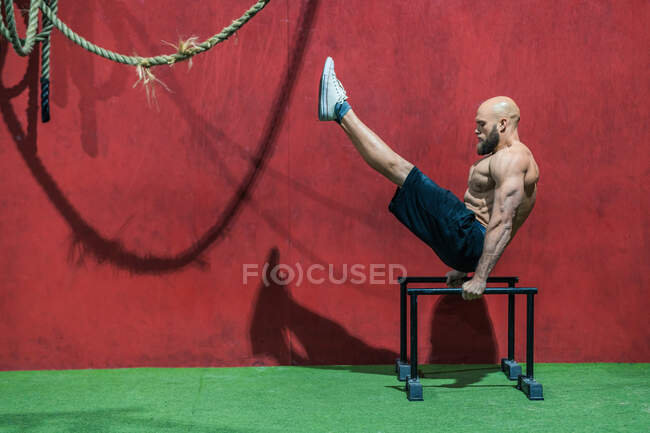 Vue latérale du sportif barbu faisant de l'exercice sur des barres contre un mur rouge pendant l'entraînement dans la salle de gym — Photo de stock