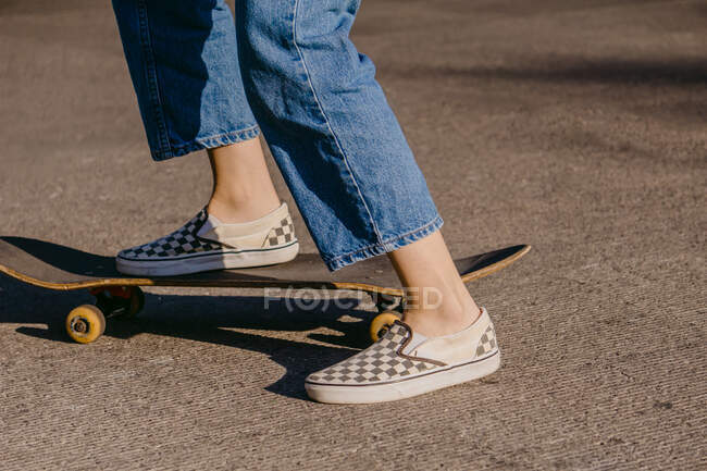 Vista laterale del raccolto skateboarder irriconoscibile in abbigliamento casual equitazione skateboard sulla passerella nella giornata di sole — Foto stock