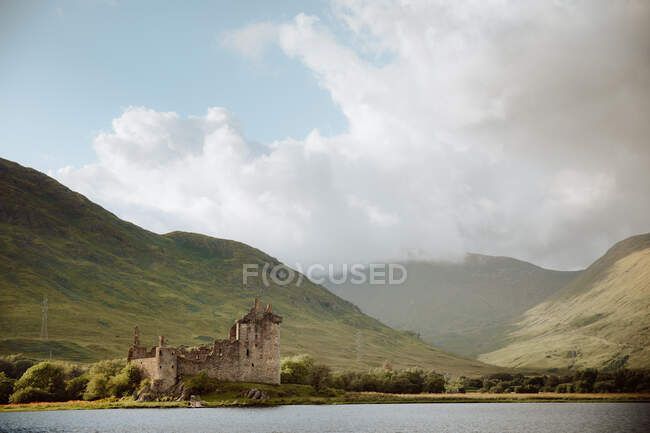 Beschädigte alte Burg am Ufer des ruhigen Sees gegen grasbewachsene Hügel auf dem Land am bewölkten Tag in Kilchurn Castle, Großbritannien — Stockfoto