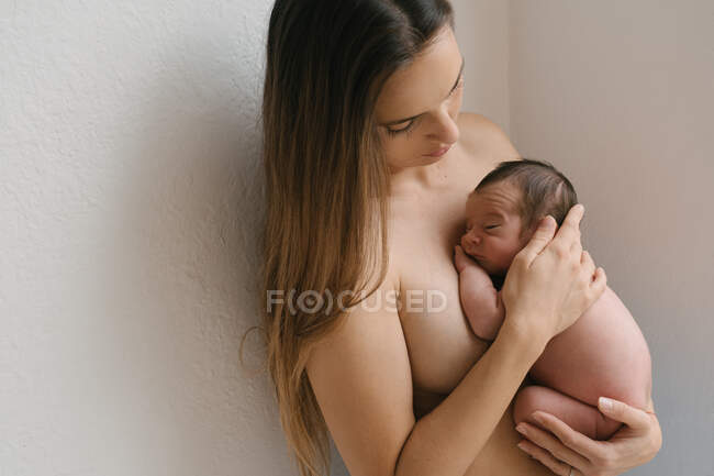 Seitenansicht einer zarten Oben-ohne-Mutter mit geschlossenen Augen, die mit einem niedlichen nackten Säugling in der Nähe der Hauswand steht — Stockfoto