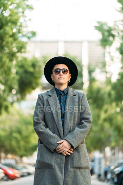 Young transgender person in classy coat and hat looking away in daylight — Stock Photo