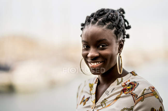 Belle dame afro-américaine élégante et coûteuse avec des tresses africaines regardant sérieusement la caméra dans le parc — Photo de stock