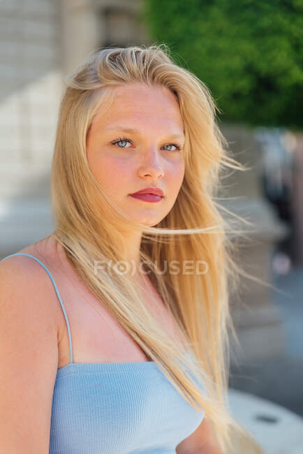 Blonde female in summer outfit sitting in street on sunny day and looking at camera while enjoying summer — Stock Photo