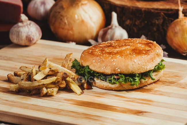 Hamburgers appétissants aux légumes placés sur une planche de bois avec frites dans la cuisine — Photo de stock