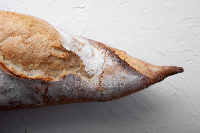 Apetitiva baguette recién horneada con corteza crujiente colocada sobre una mesa blanca - foto de stock