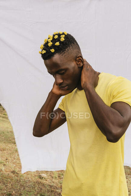 Bello afroamericano maschio con fiori gialli in capelli che toccano il collo e guardando verso il basso su sfondo bianco — Foto stock