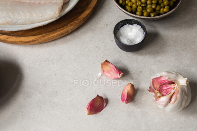 Desde arriba ver los dientes de ajo maduro y un tazón pequeño de sal colocado en la mesa de la cocina durante la preparación de los alimentos - foto de stock