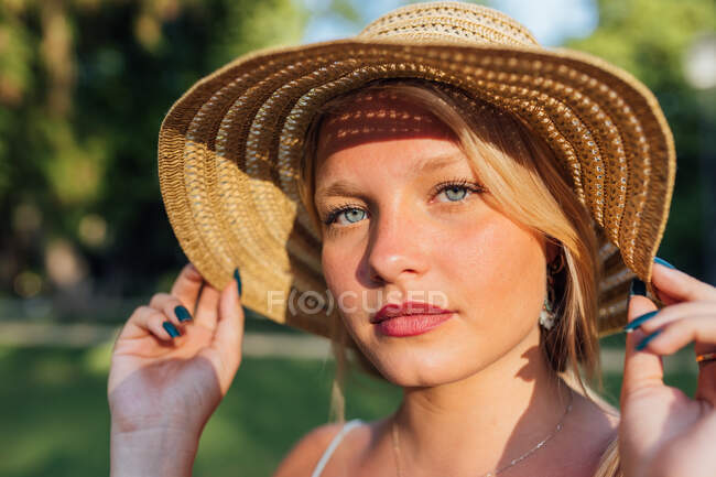 Charming female wearing straw hat looking at camera on sunny day in city street in summer — Stock Photo