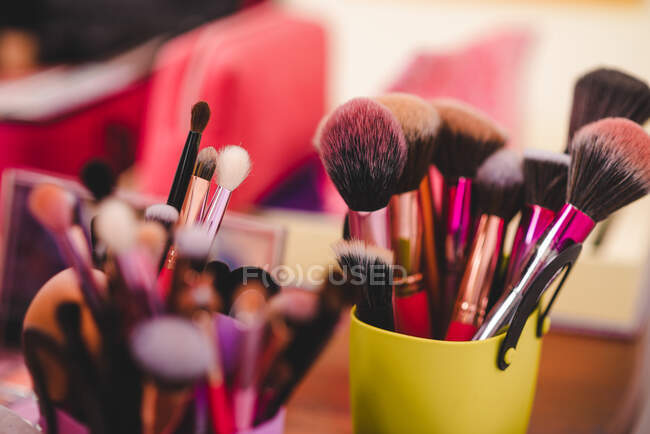 Weicher Fokus der Tasse mit verschiedenen Make-up-Pinseln auf dem Tisch mit Kosmetik im Salon platziert — Stockfoto