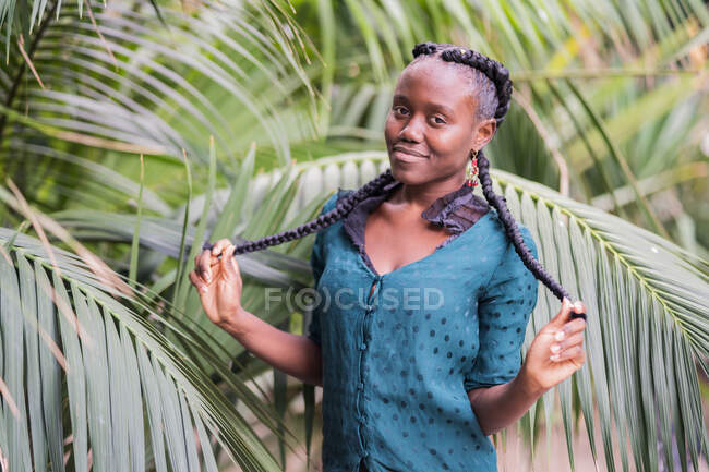 Stylish charming beautiful African American lady with African braids looking at camera in green park — Stock Photo
