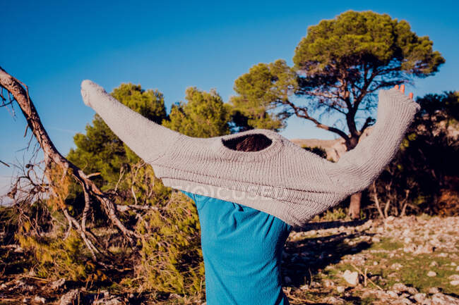 Неузнаваемый путешественник надевает вязаный свитер, стоя в горах в солнечный день — стоковое фото