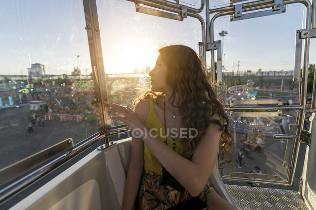 Mujer positiva sentada en cabina de rueda de observación y disfrutando del paseo mientras se divierten en el parque de atracciones y mirando hacia otro lado - foto de stock