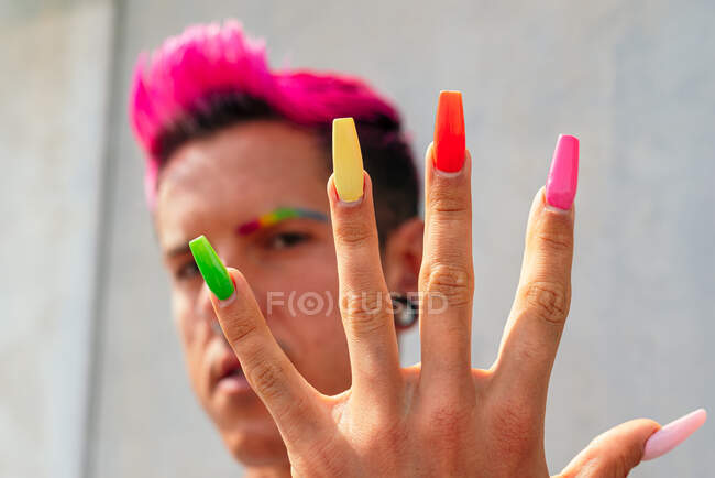Confiante gay masculino com longo colorido unhas olhando para câmera no rua no ensolarado dia — Fotografia de Stock
