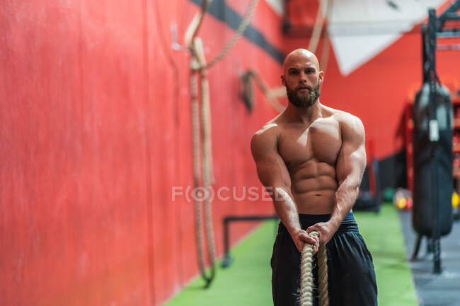 Strong sportsman pulling rope with heavy weights during intense workout in contemporary gym — Stock Photo