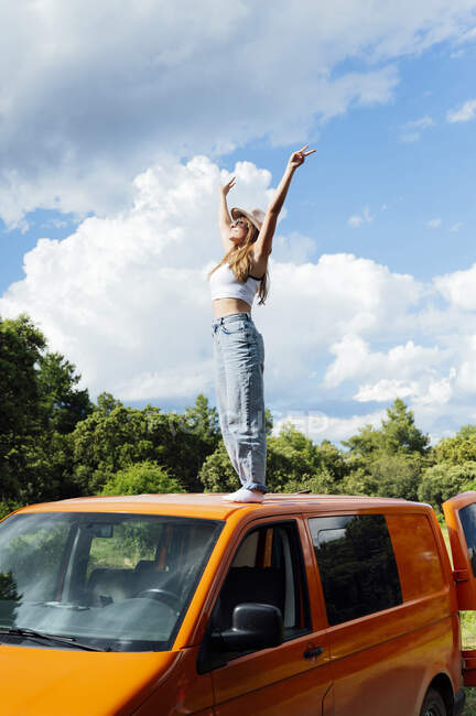 Side view of carefree female traveler standing on roof on van parked in nature in summer — Stock Photo