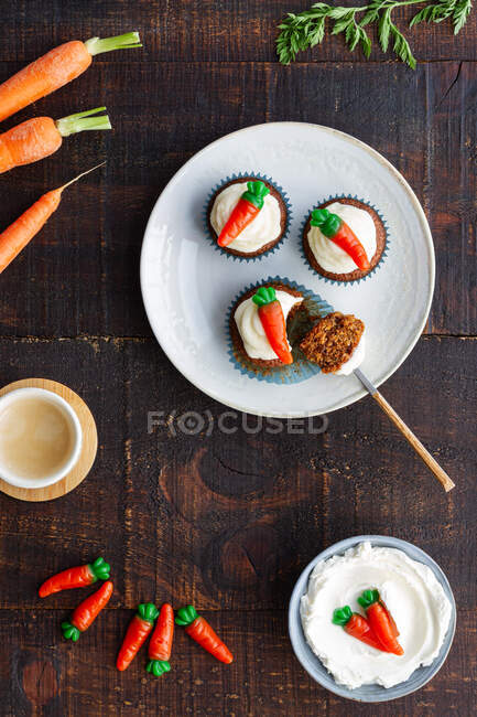 Vista superior del plato con deliciosos cupcakes de verduras con pequeña zanahoria dulce decoración en la parte superior colocado en la mesa de madera - foto de stock