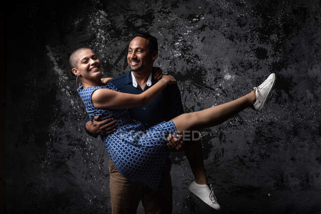 Cheerful man holding girlfriend and having fun in dark studio — Stock Photo