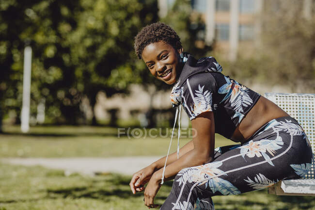Joven fitness mujer afroamericana descansando después de hacer ejercicio en el banco del parque - foto de stock