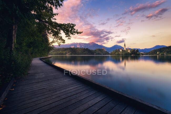 Majestic scenery of long wooden boardwalk near calm pond under sundown sky in summer in Slovenia — Stock Photo