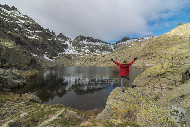 Vue arrière de l'homme anonyme en vêtements de dessus debout sur des pierres près du lac Laguna Grande au milieu des montagnes de la chaîne Sierra de Gredos à Avila, Espagne — Photo de stock