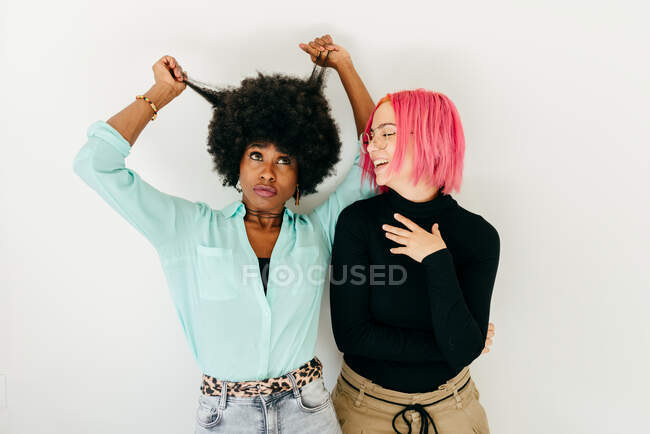 Fröhliche junge Frau mit rosa Haaren und afroamerikanische Freundin in stilvollem Outfit stehen zusammen auf weißem Hintergrund — Stockfoto