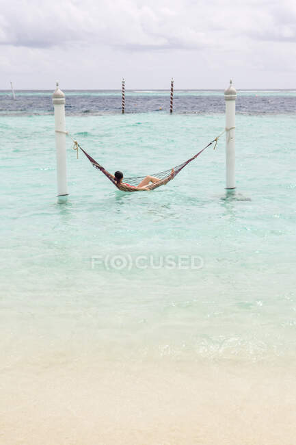 Женщина в красном купальнике лежит в гамаке и качается по океанской волне, расслабляясь на Мальдивах в пасмурный день. — стоковое фото
