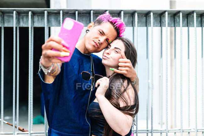 Na moda gay masculino e elegante mulher tomando auto retrato no celular enquanto abraçando no rua — Fotografia de Stock