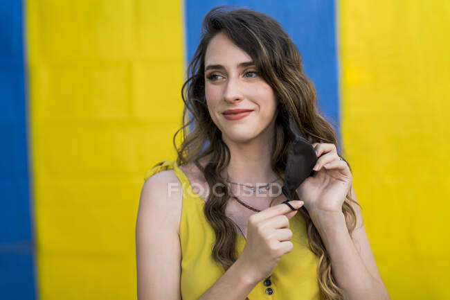 Content female with wavy hair wearing protective mask during coronavirus in city looking away on two colored background — Stock Photo