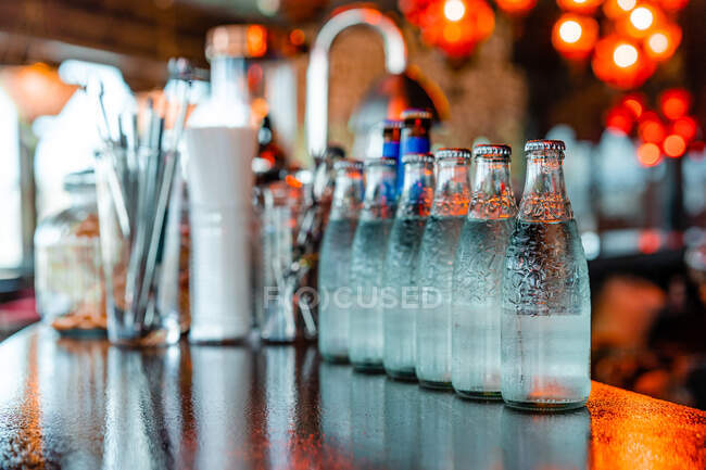 Bottiglie di vetro con acqua fredda rinfrescante poste in fila su bancone in legno in bar — Foto stock