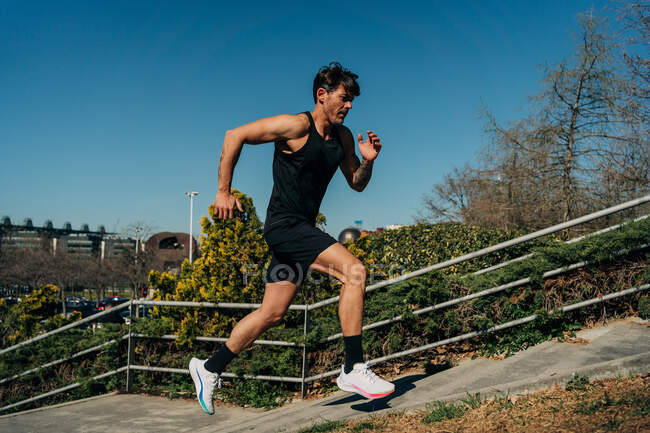 Vista laterale del jogger maschile attivo in abbigliamento sportivo che corre sulle scale durante l'allenamento sotto il cielo blu — Foto stock
