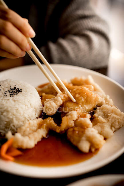 Mano di donna seduta a tavola e che mangia con le bacchette Farina di pesce fritta cinese dal piatto in ceramica bianca — Foto stock