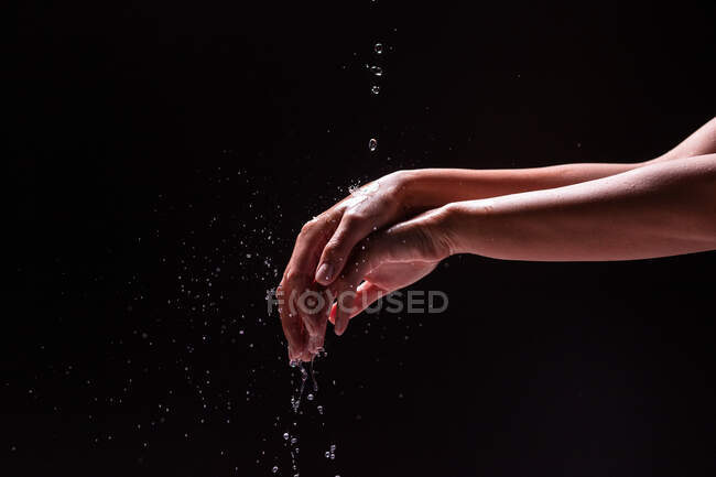 Vista de la cosecha de la mujer anónima lavándose las manos con agua salpicada contra fondo negro - foto de stock