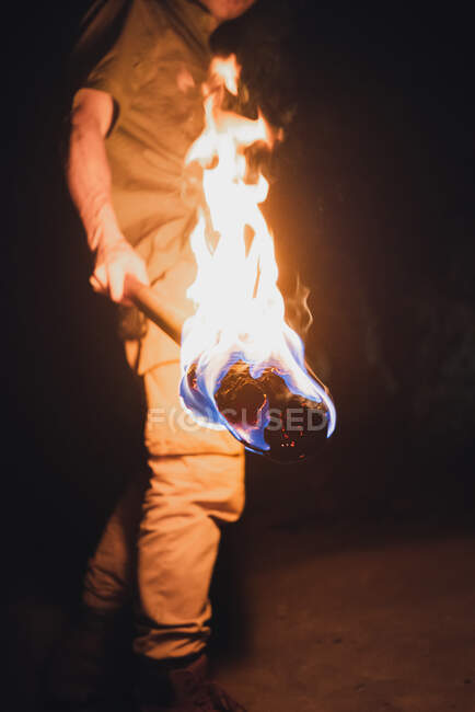 Side view of cropped anonymous male speleologist with flaming torch standing in dark narrow rocky cave while exploring subterranean environment — Stock Photo