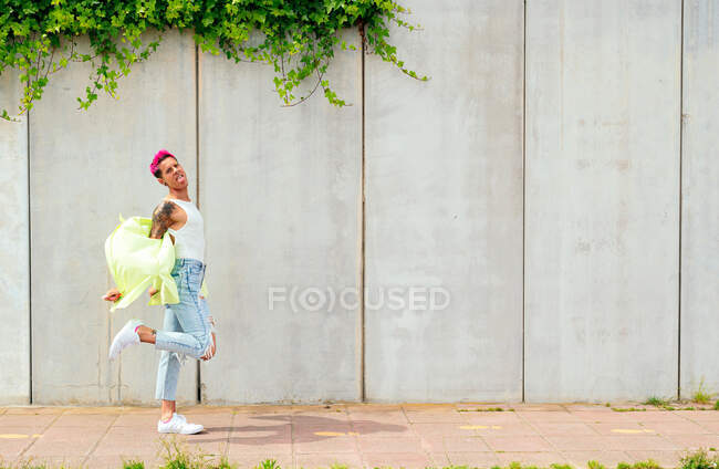 Вид сбоку мужчины-гея с розовыми волосами и татуировками, прогуливающегося по городской улице летом — стоковое фото